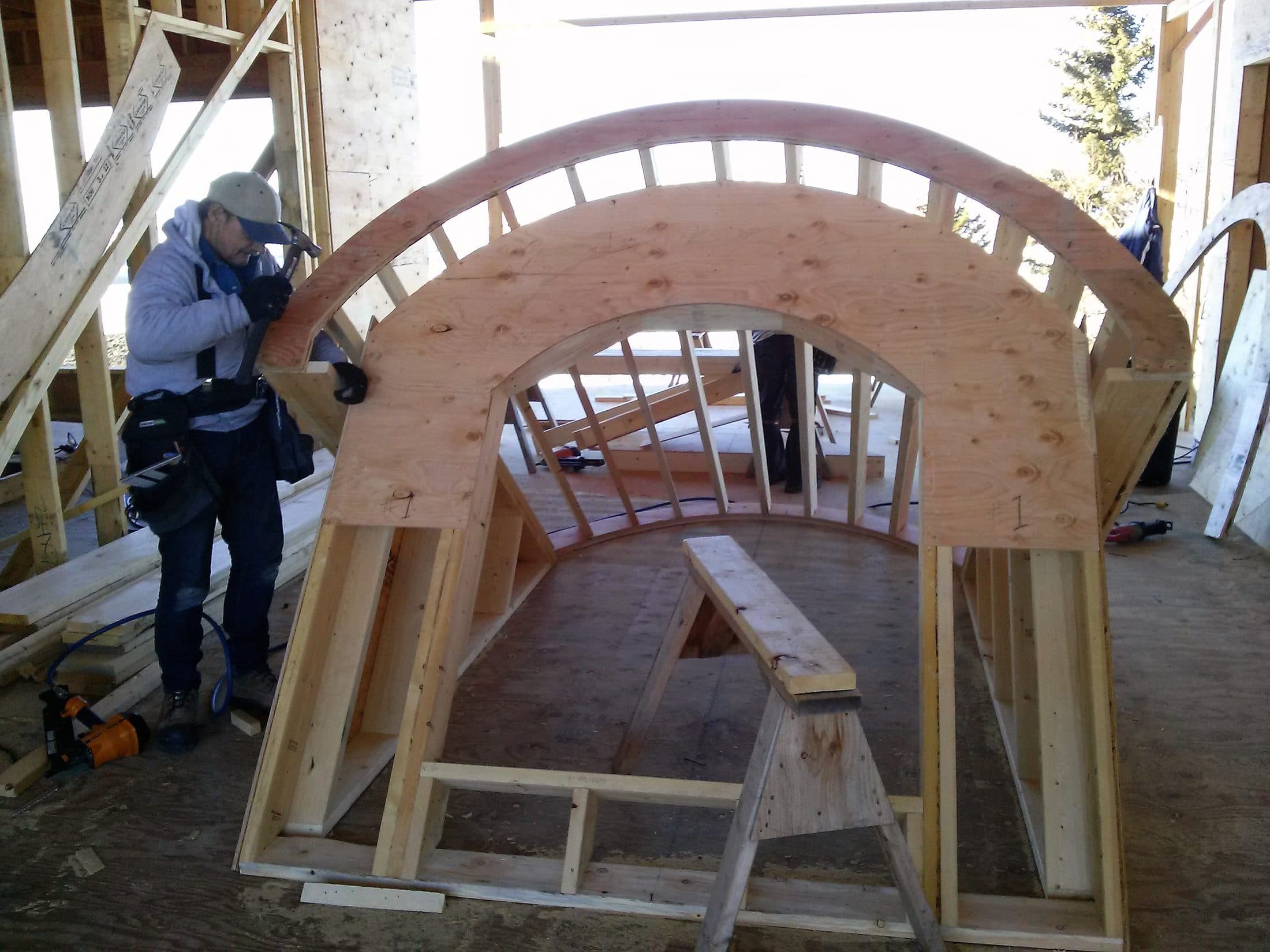Carpenter assembling a curved barrel-vault roof frame on site